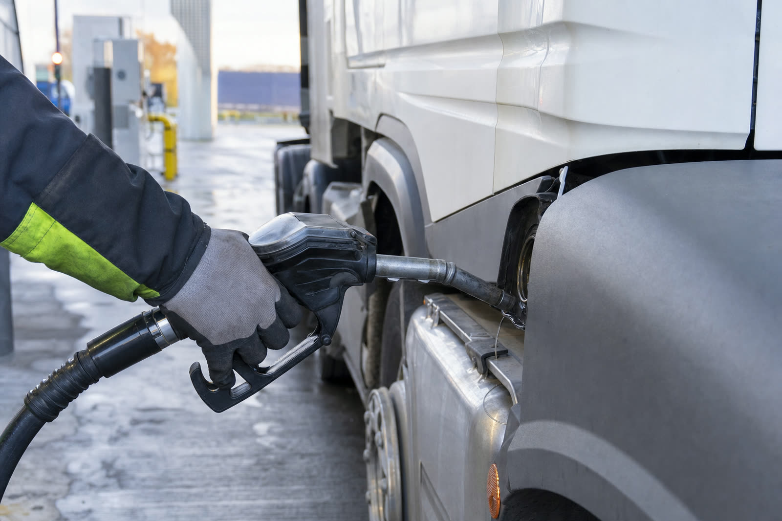 A diesel nozzle in the filler neck of a white articulated HGV at a UK truck stop in early morning light